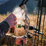 a man's hand applying Scent Assassin hunting spray on his hunting bow